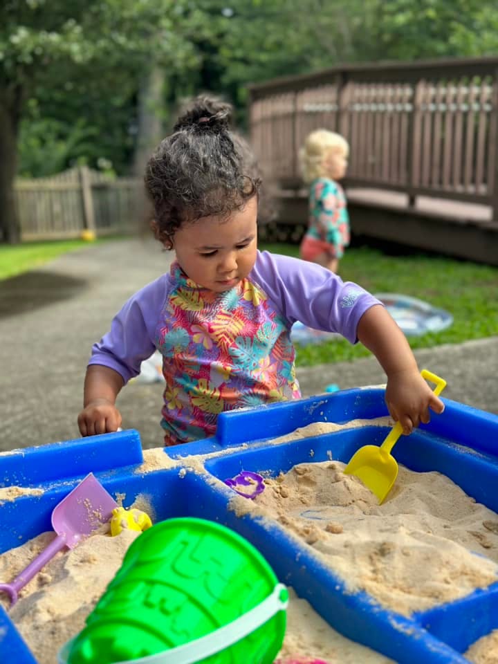 Child playing in a sandbox with a yellow shovel