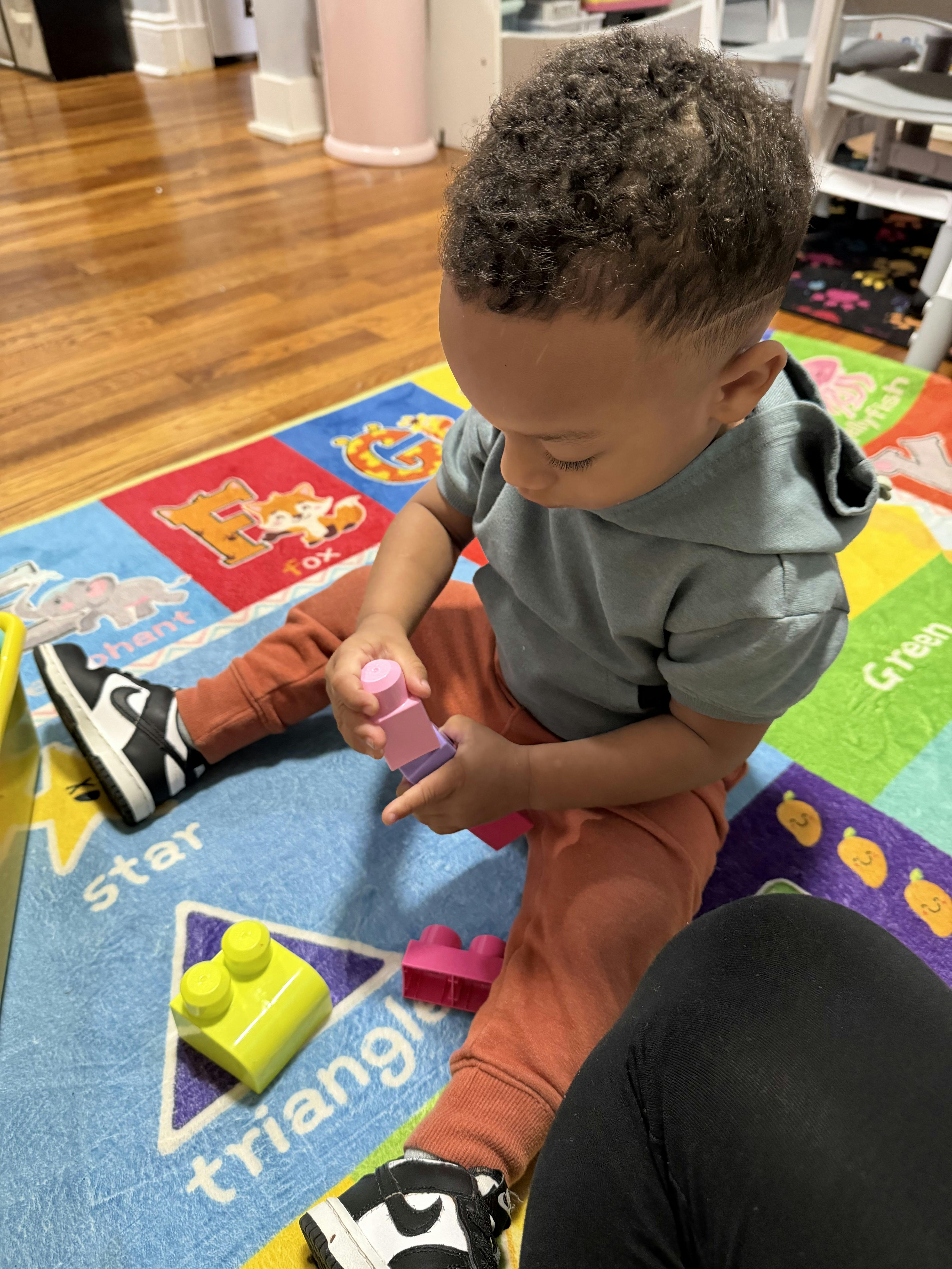 Child sitting on a colorful alphabet rug, playing with toy blocks