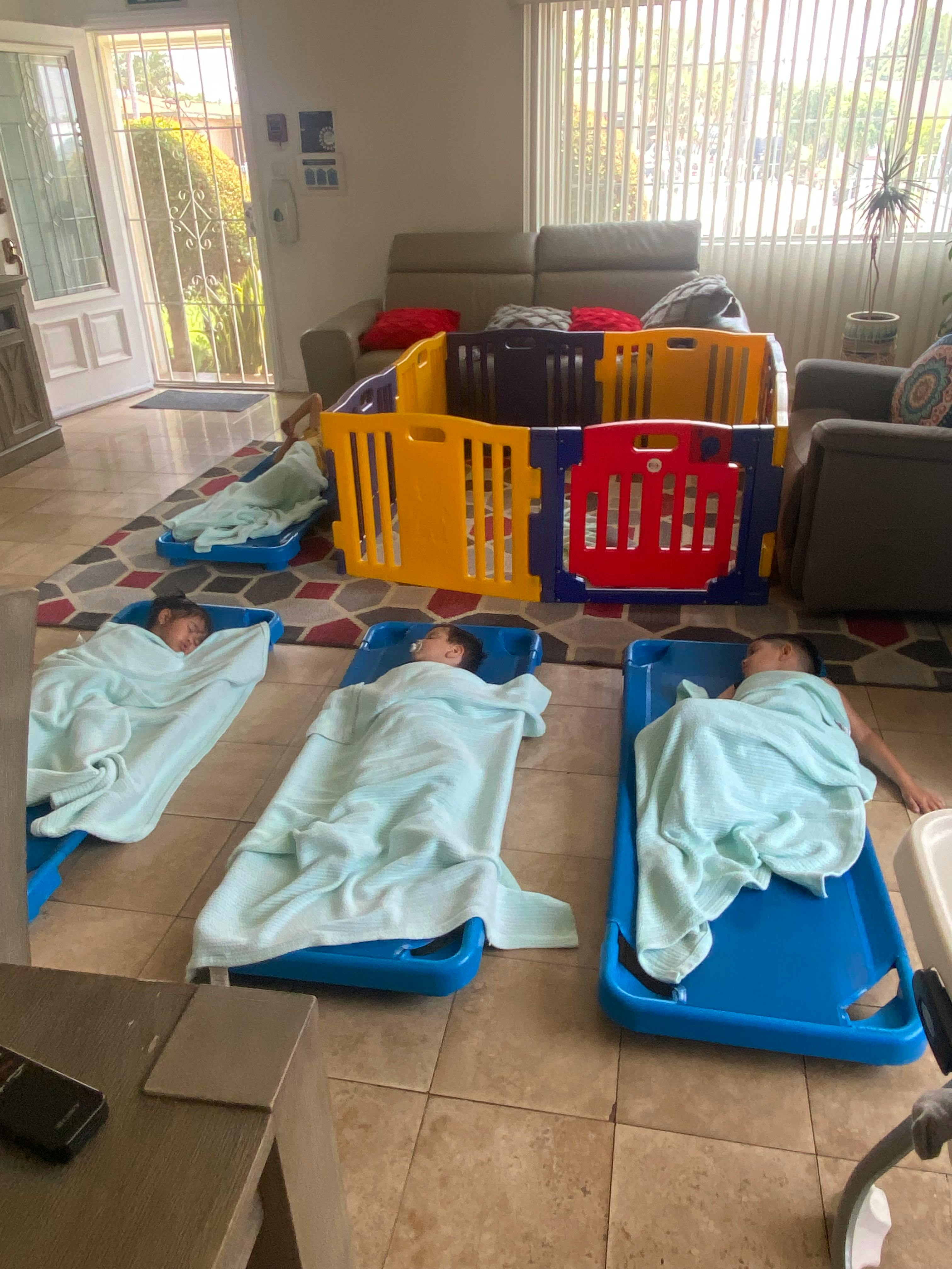 Three children sleeping on blue cots, covered with blankets