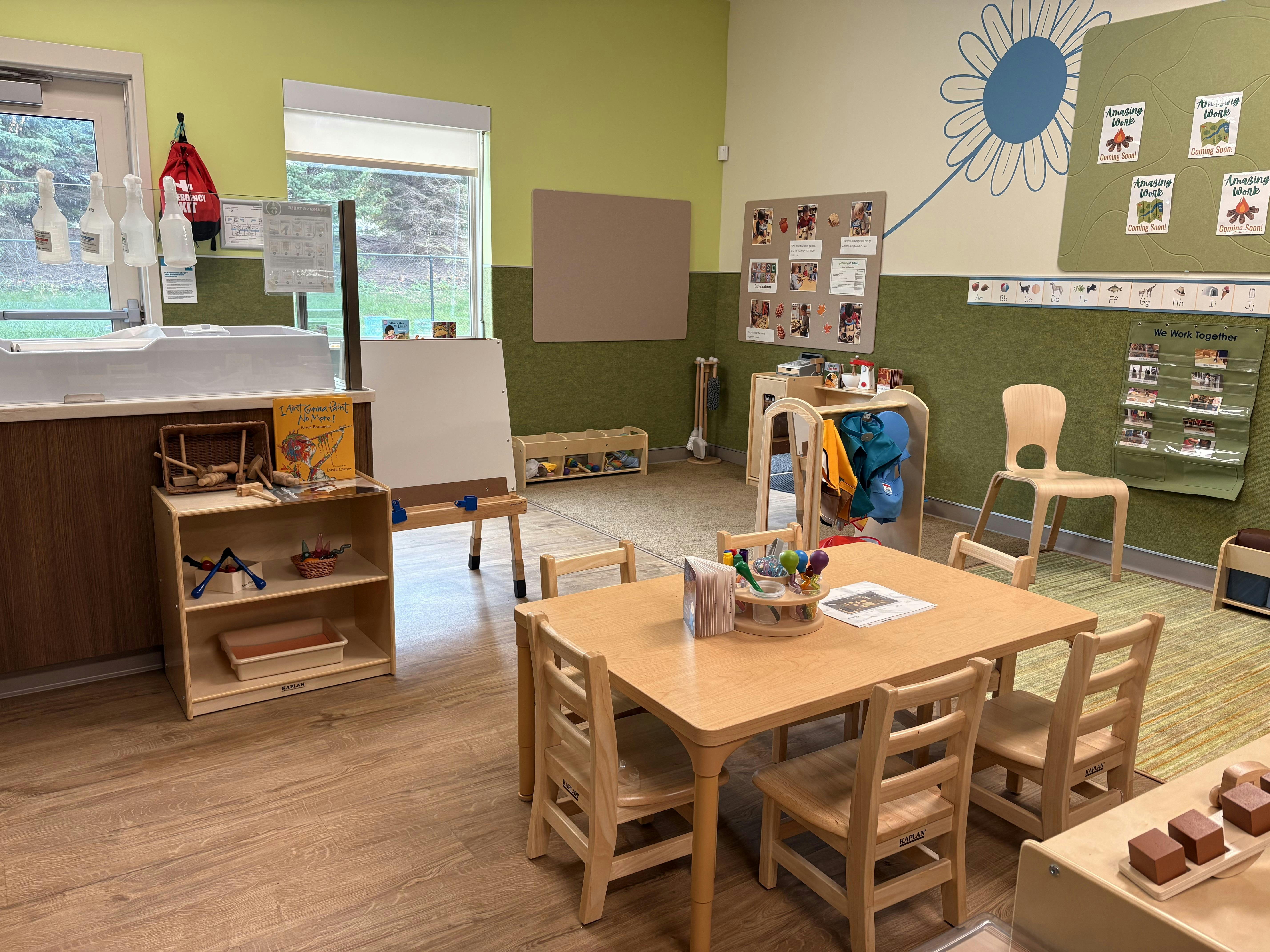 Classroom with small wooden tables and chairs, shelves, and an easel