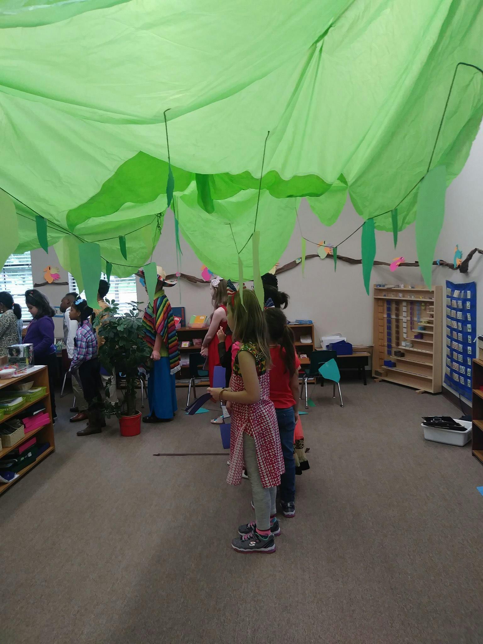 Children and adults standing in a classroom with green fabric draped overhead
