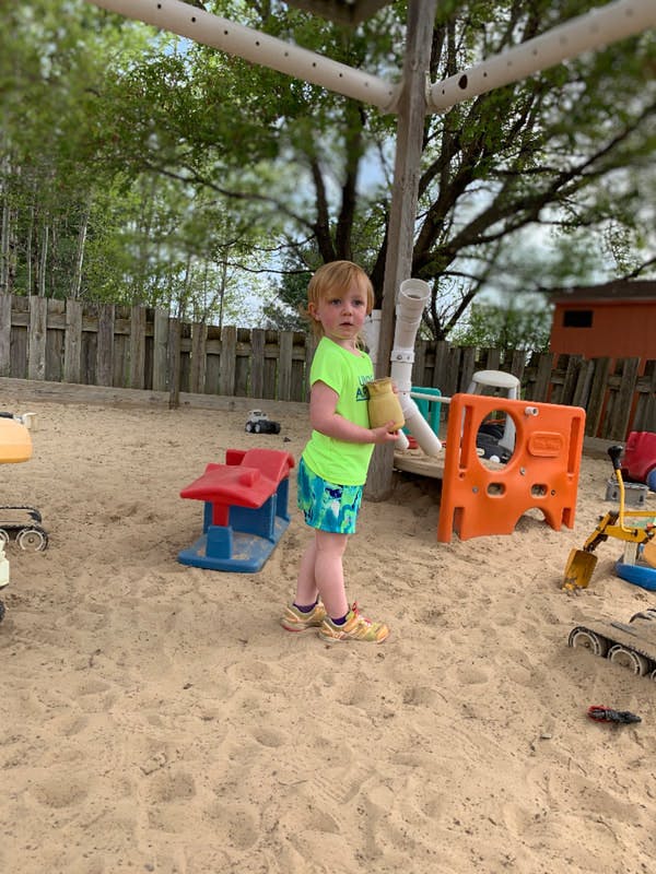 Child standing in a sandbox holding a small object