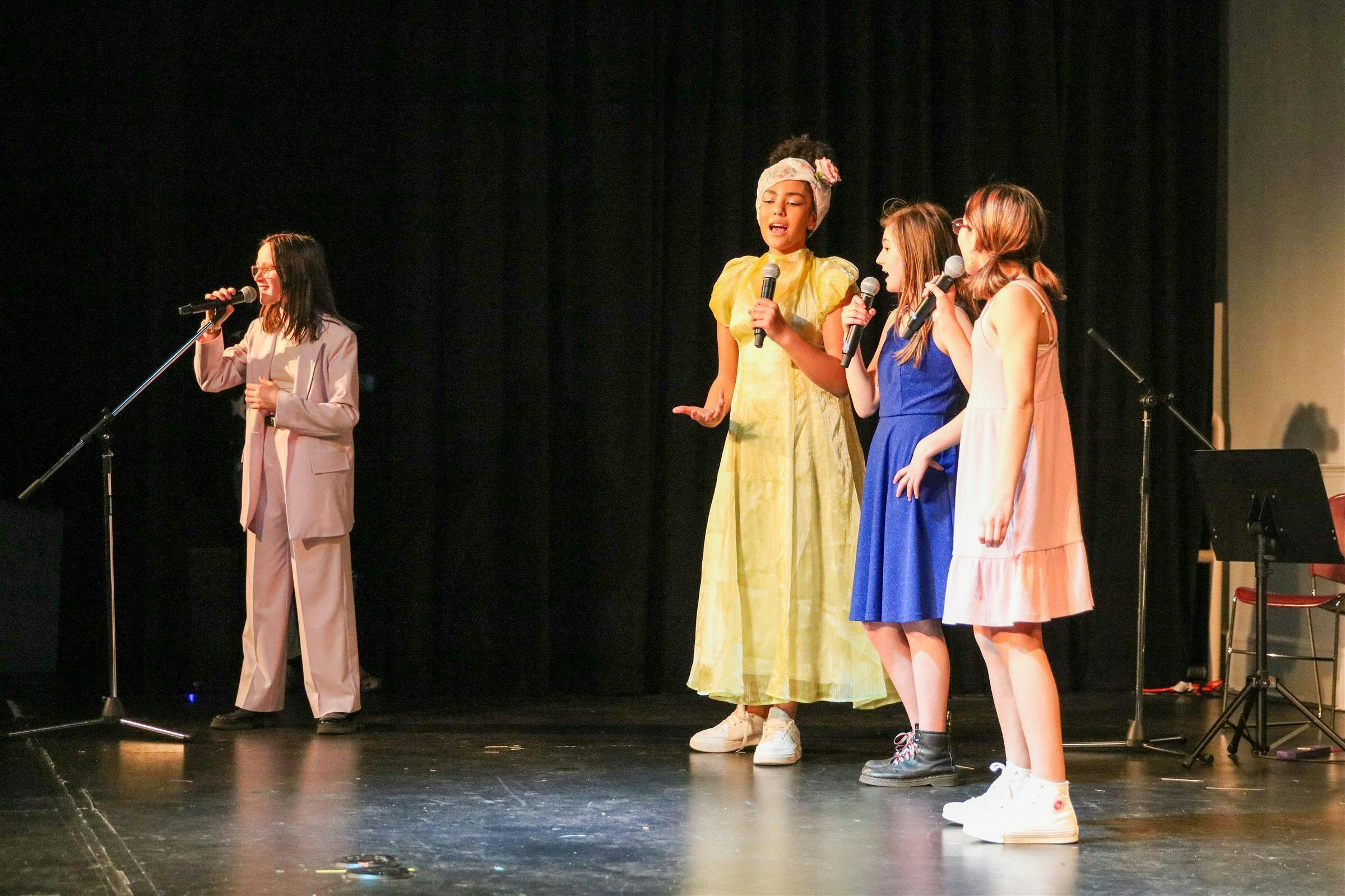Four teens singing into microphones on a stage