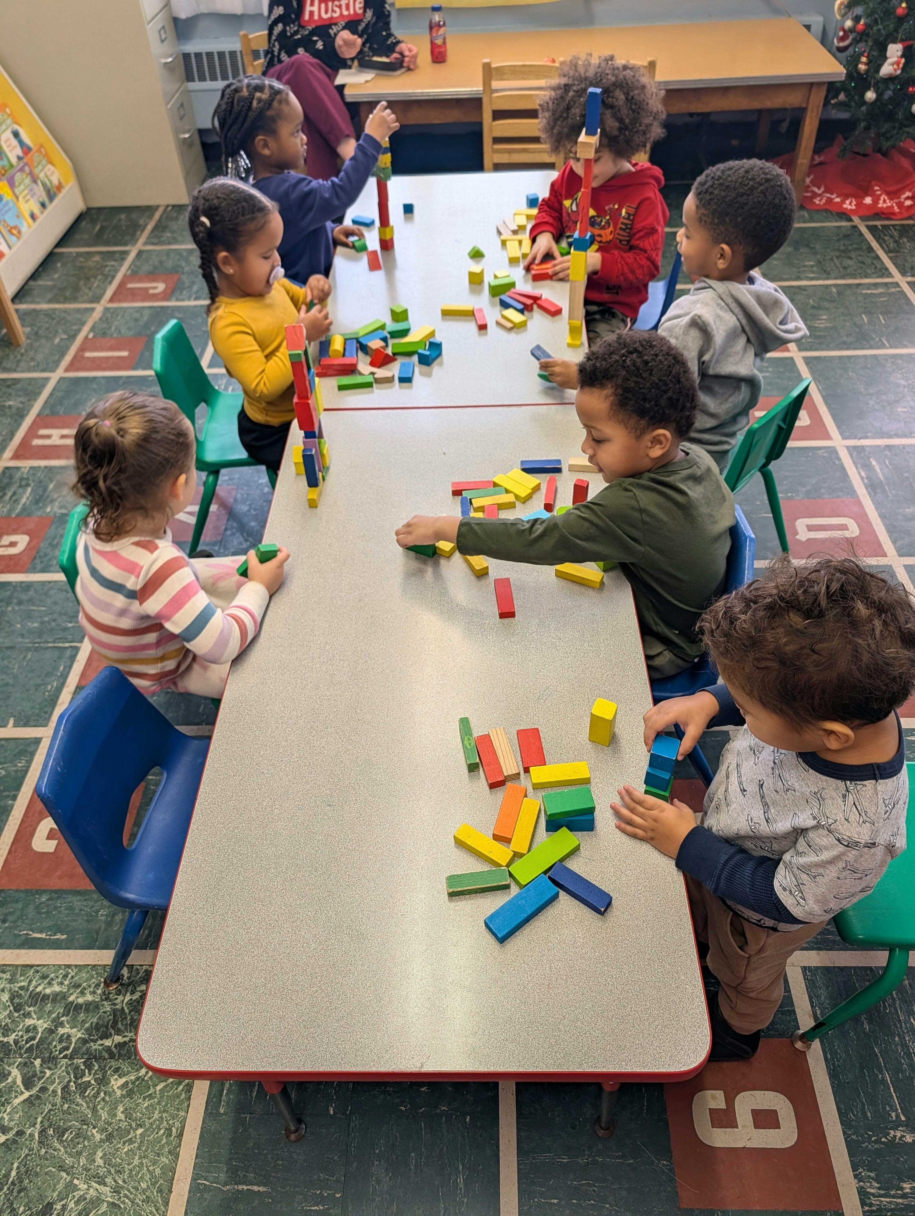 Children playing with colorful building blocks at a table in a classroom