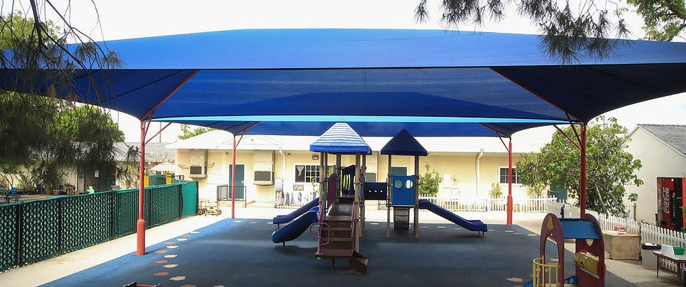 Playground with slides and climbing structures under a large blue shade canopy