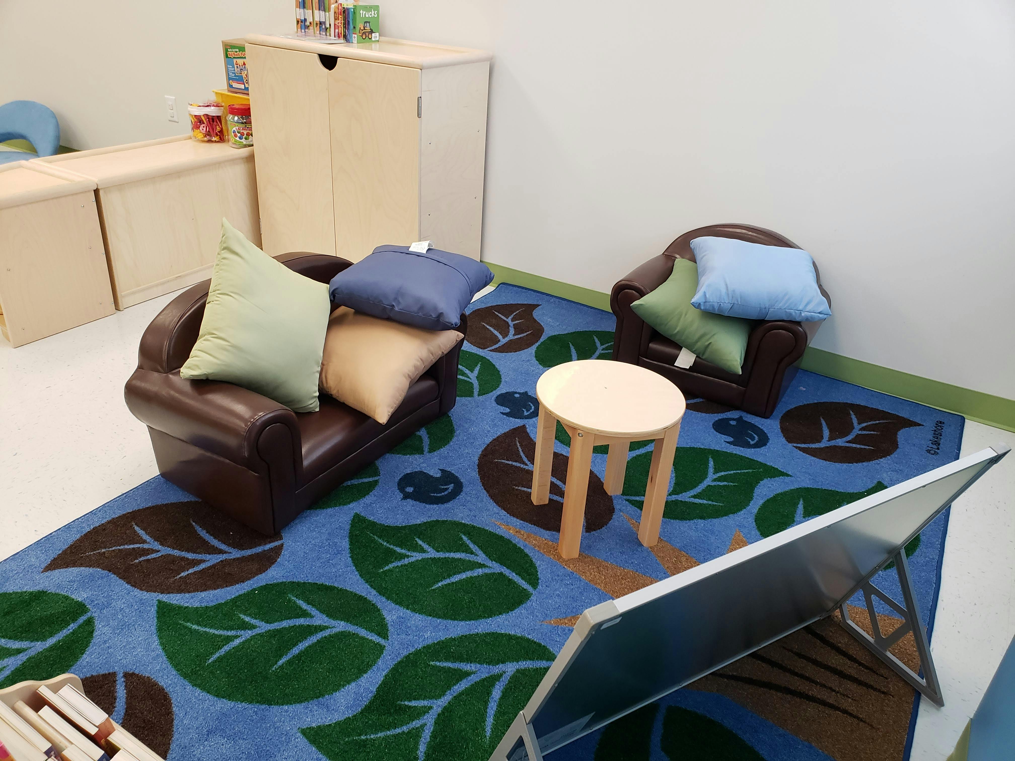 Small chairs and a table on a blue rug with leaf patterns in a classroom