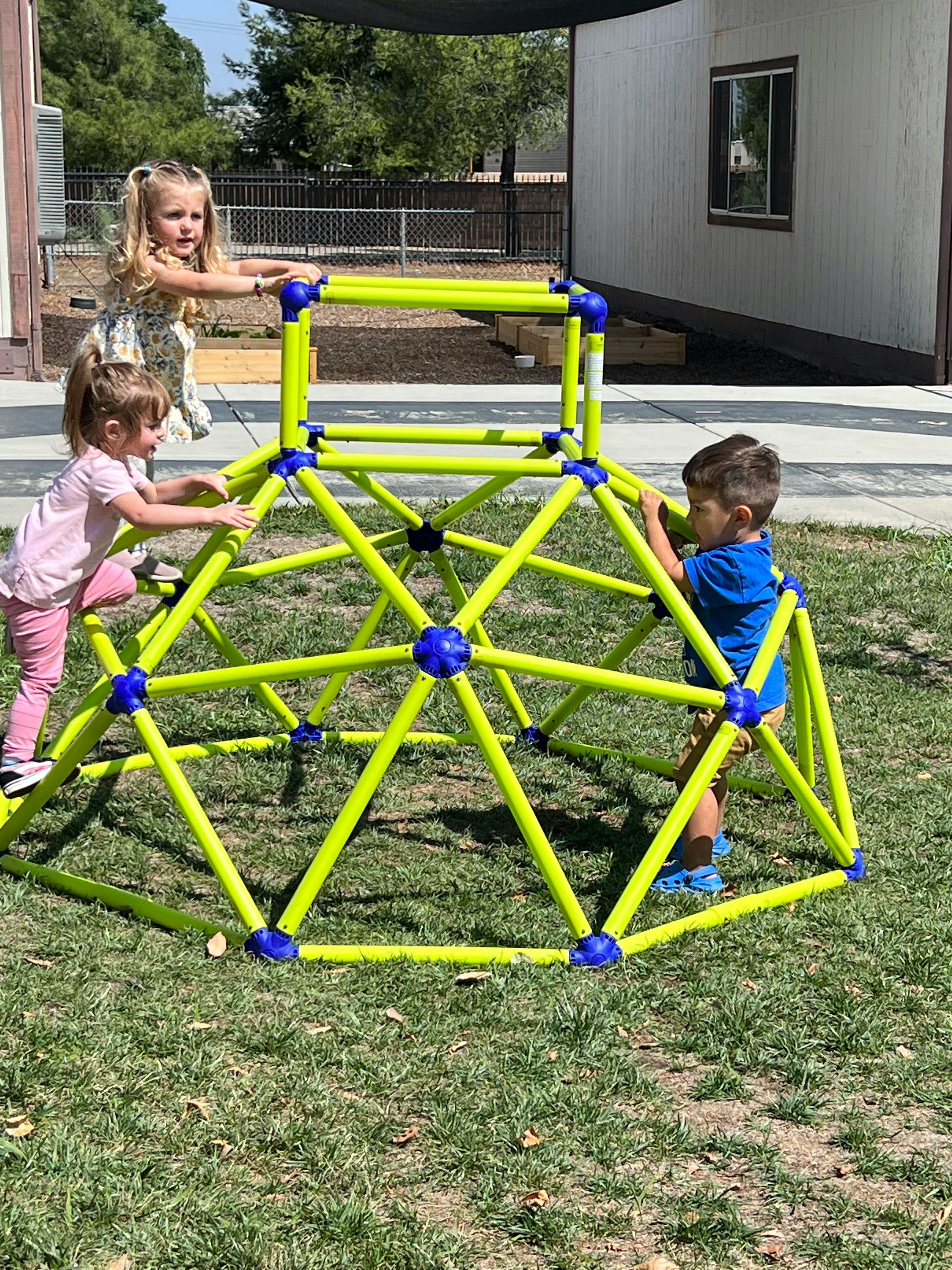 Three children playing on a green climbing dome on grass