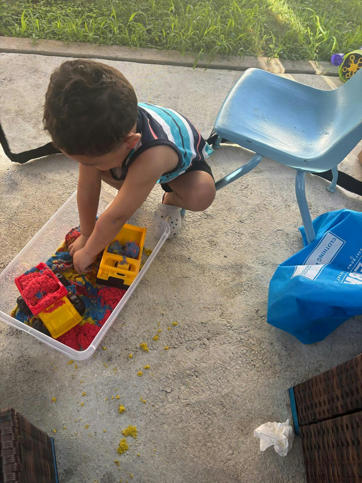 Child playing with toy trucks and kinetic sand in a plastic bin