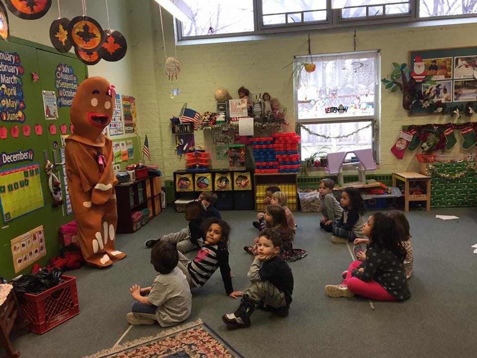 Person in gingerbread costume with children sitting on floor in classroom