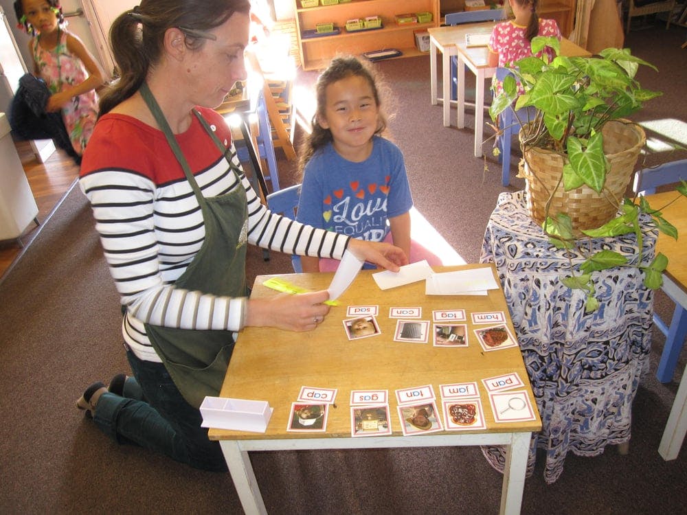 Adult and child sorting cards at a small table in a classroom