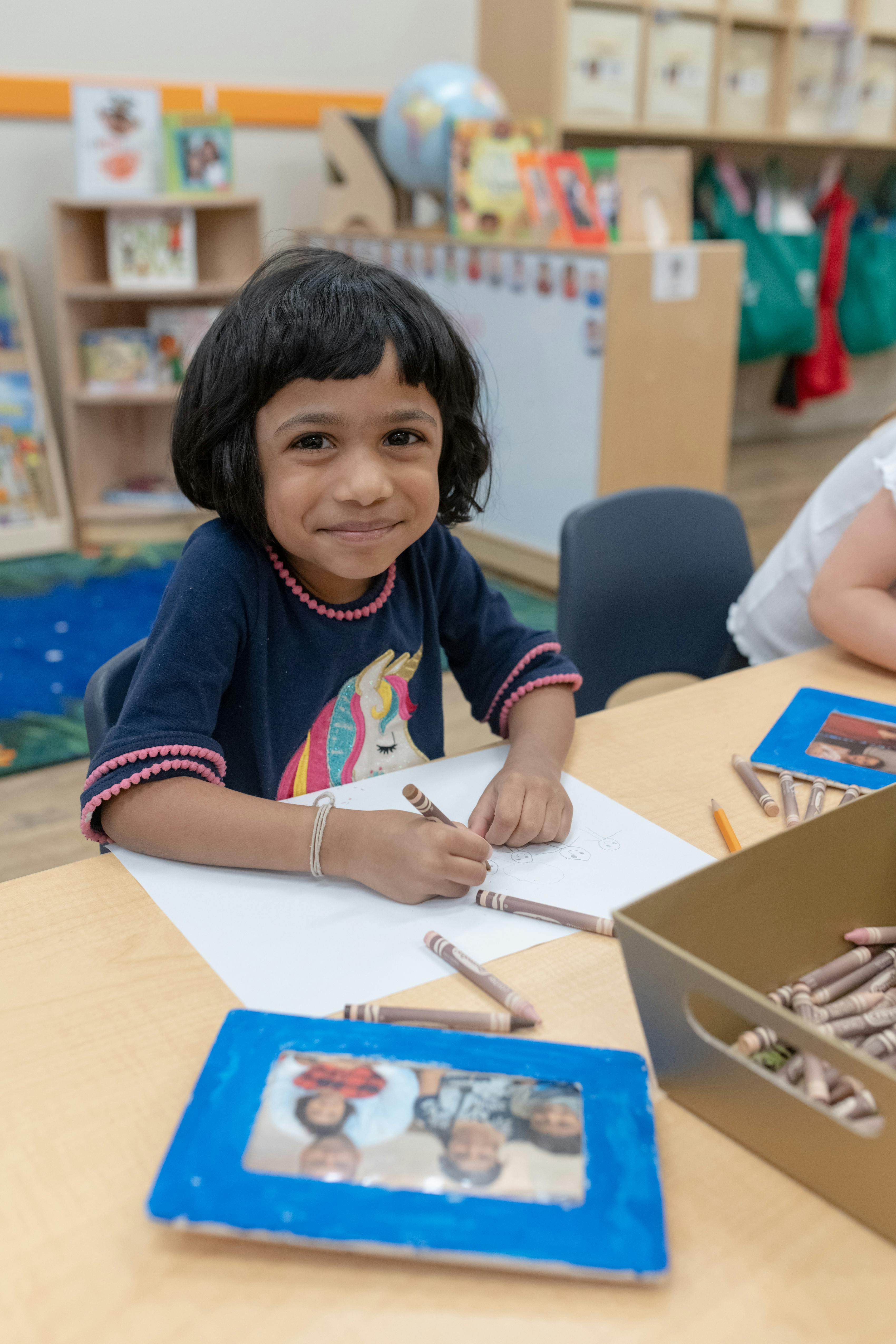 Child drawing with crayons at a table in a classroom