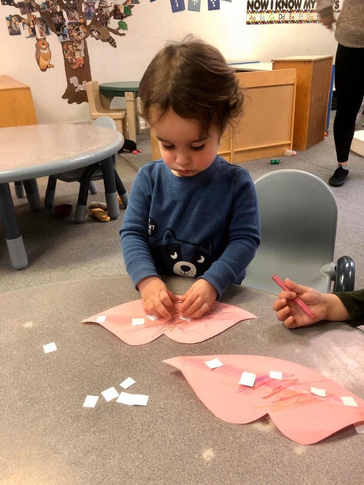 Child doing a craft with pink paper cutouts and small white squares