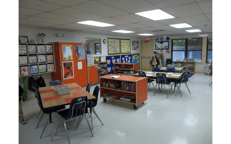 Classroom with child-sized tables and chairs, shelves, and artwork on walls
