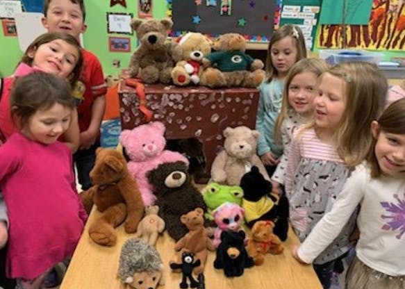Children gathered around a table with many stuffed animals