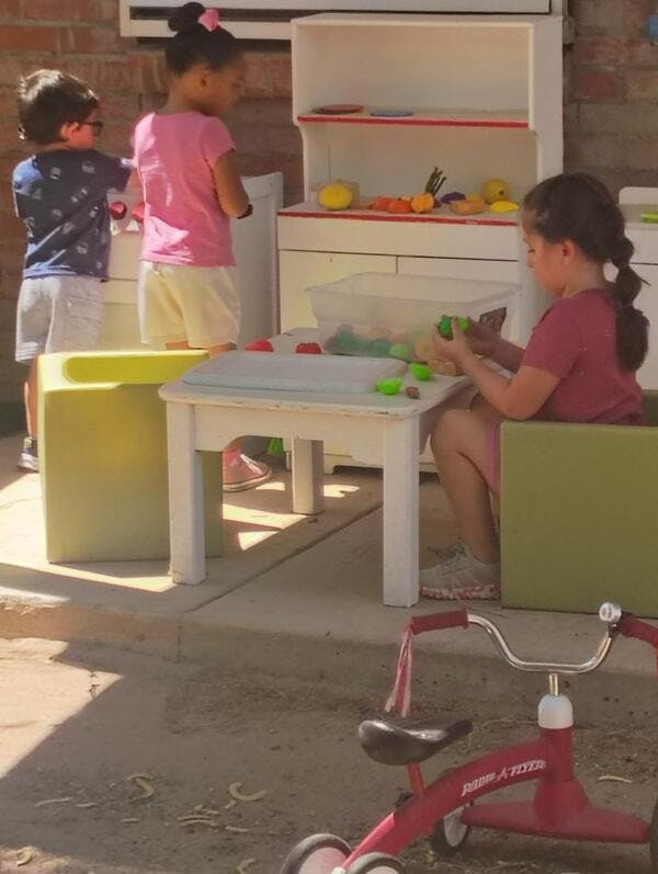 Three children playing with toy kitchen equipment outdoors