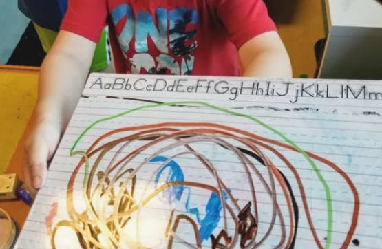 Child drawing on a whiteboard with alphabet letters at the top