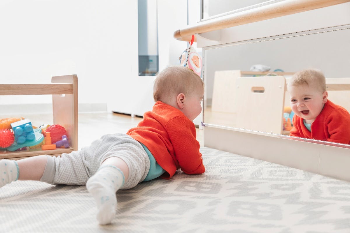 Child crawling on floor looking at reflection in mirror