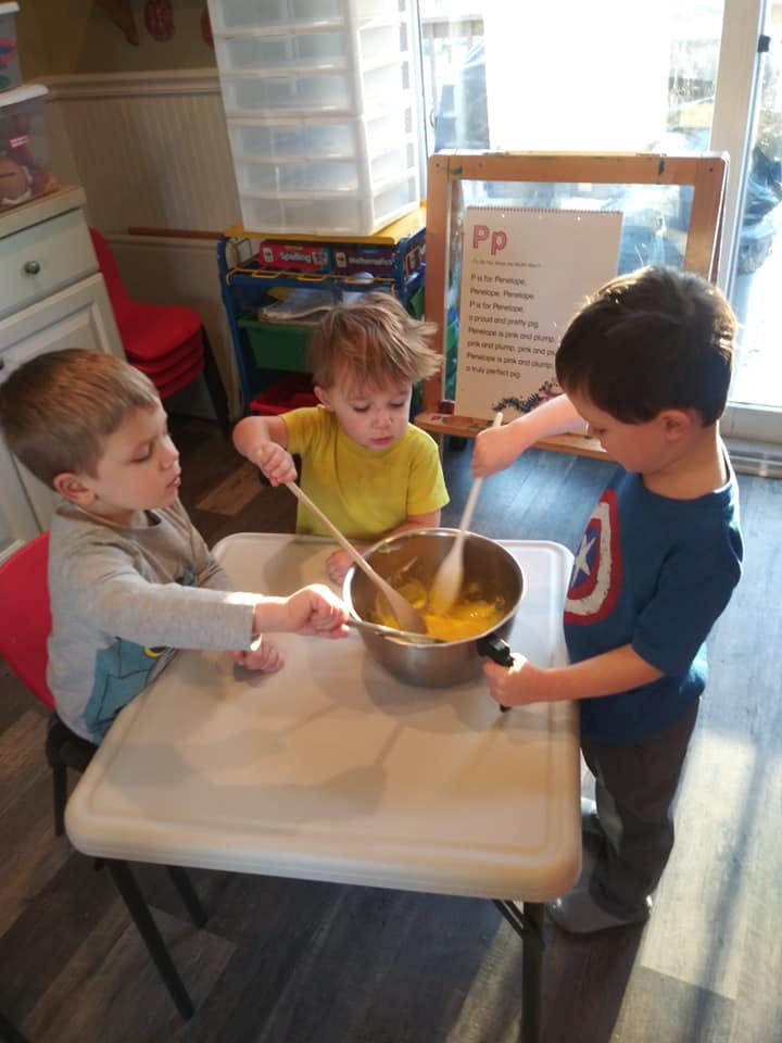 Three children mixing ingredients in a bowl on a table