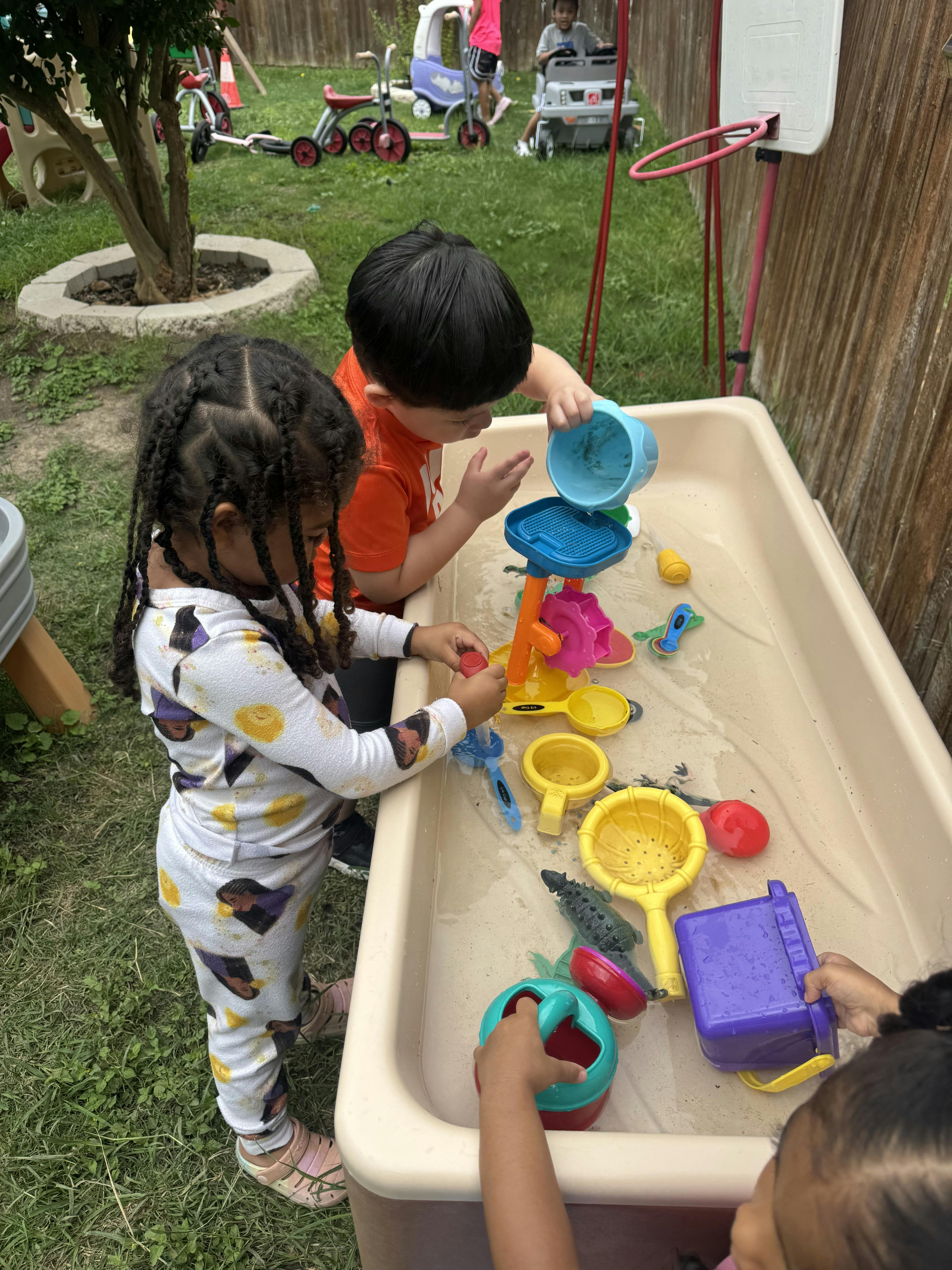 Children playing with water toys at a sensory table in a yard