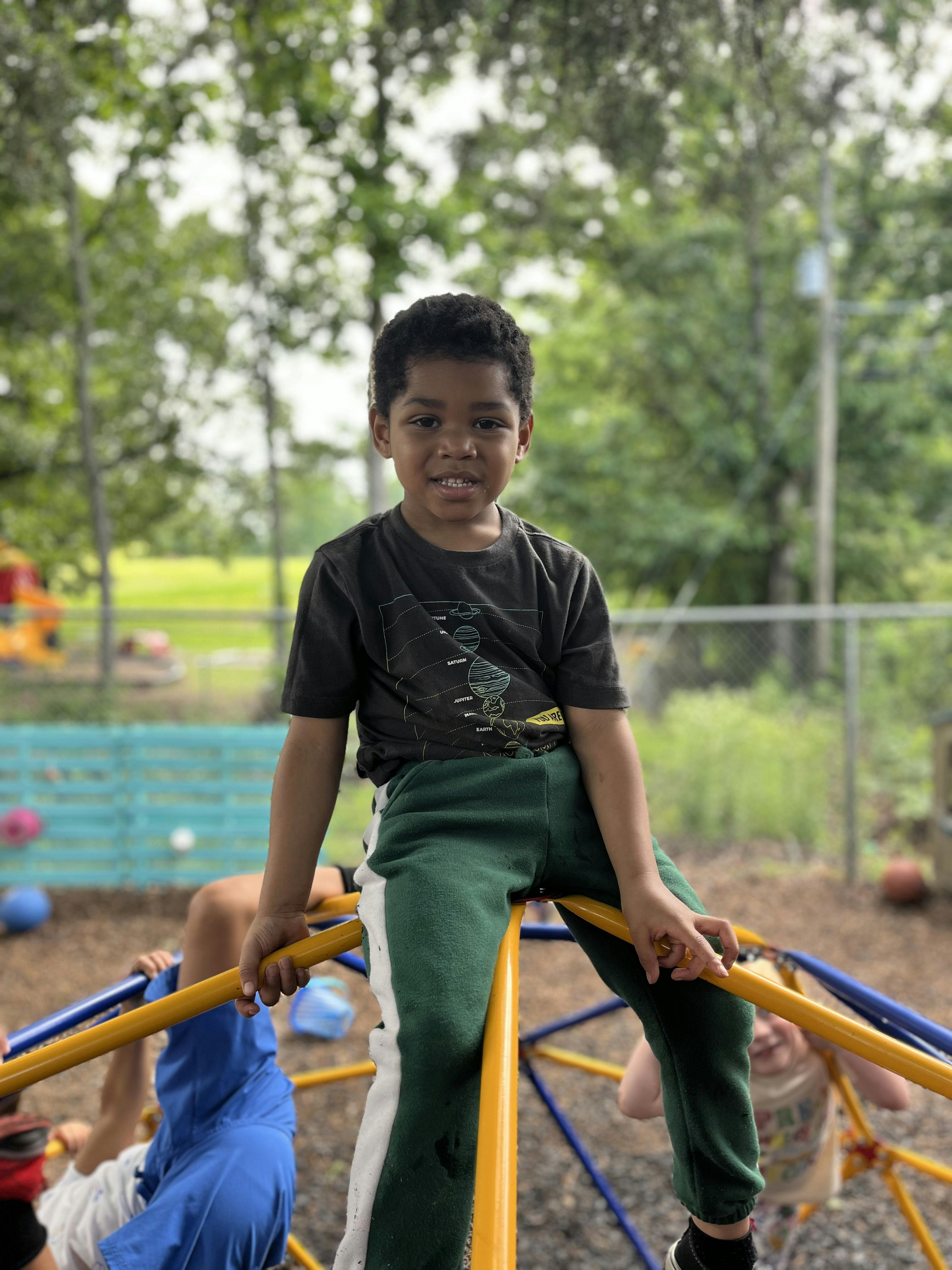 Child sitting on a yellow climbing dome on a playground
