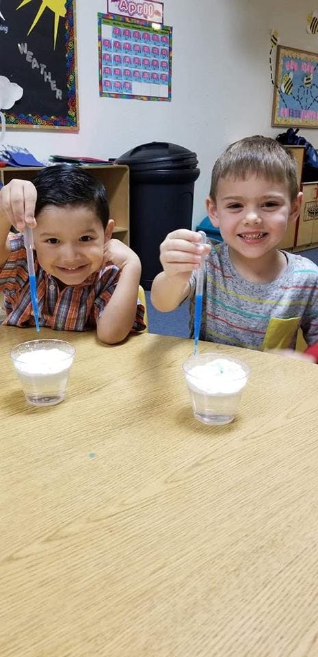 Two children holding pipettes over cups in a classroom