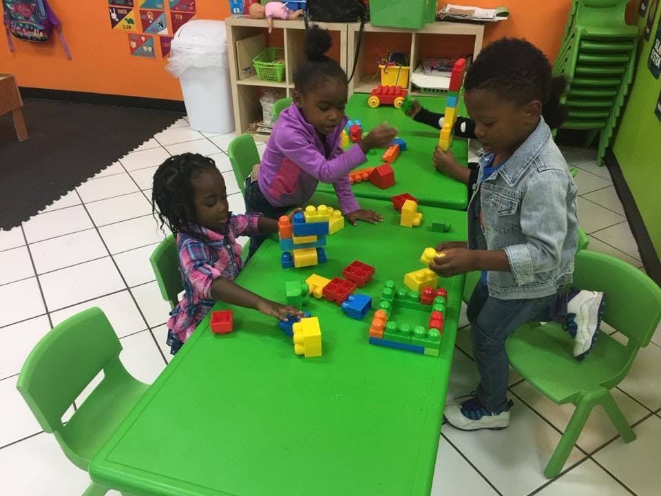 Three children playing with colorful building blocks at a green table