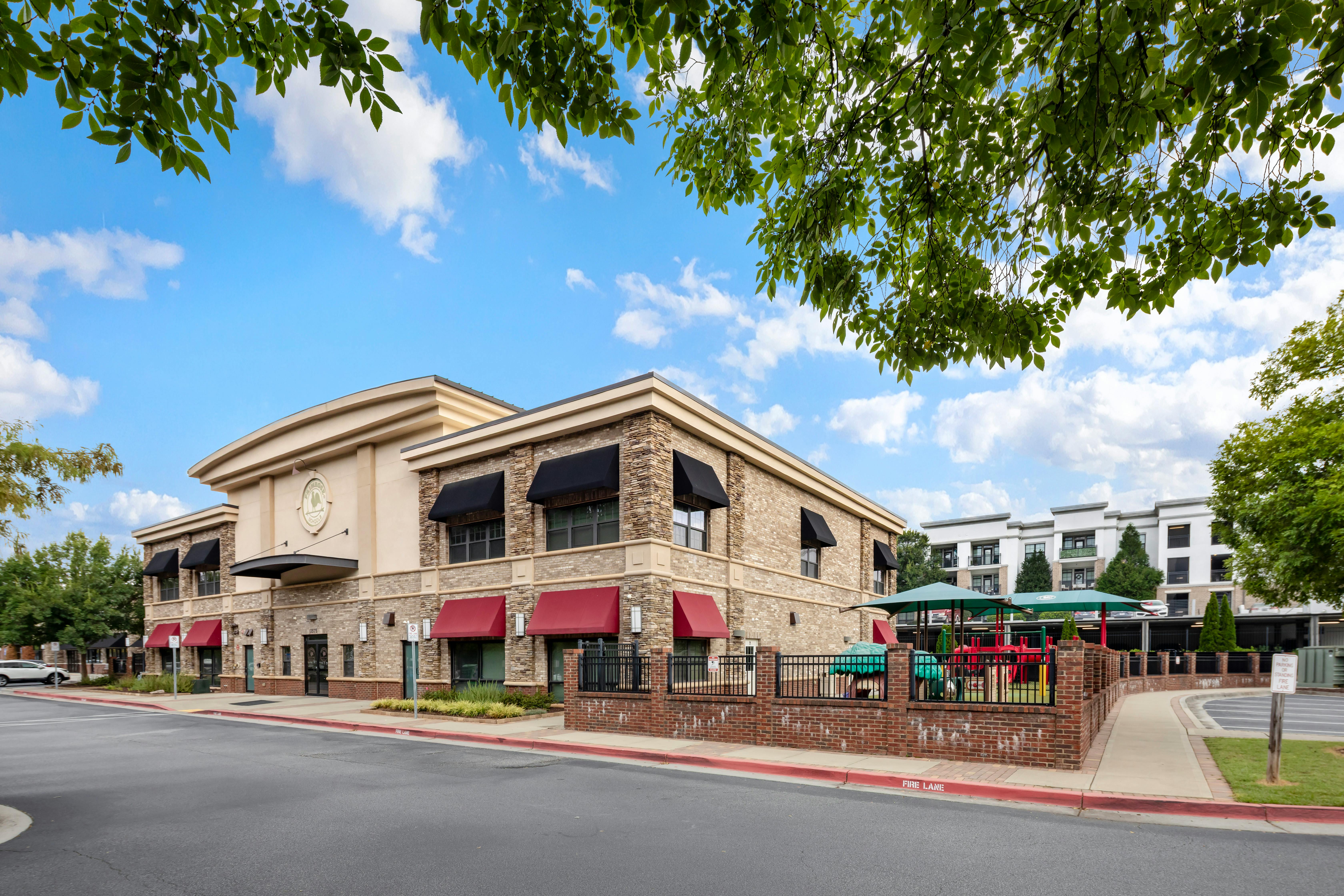 Building with stone and stucco exterior, red and black awnings, and a playground area