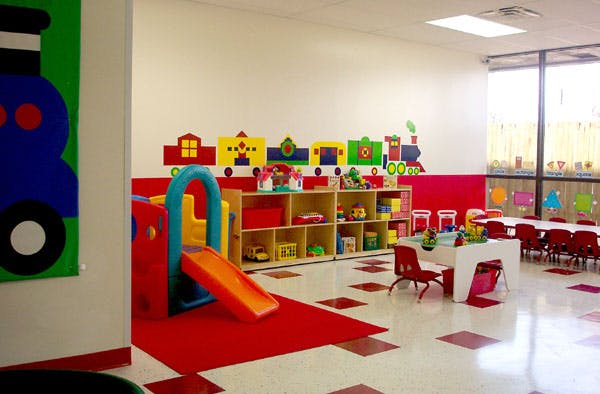 Playroom with a slide, shelves of toys, and small tables with chairs