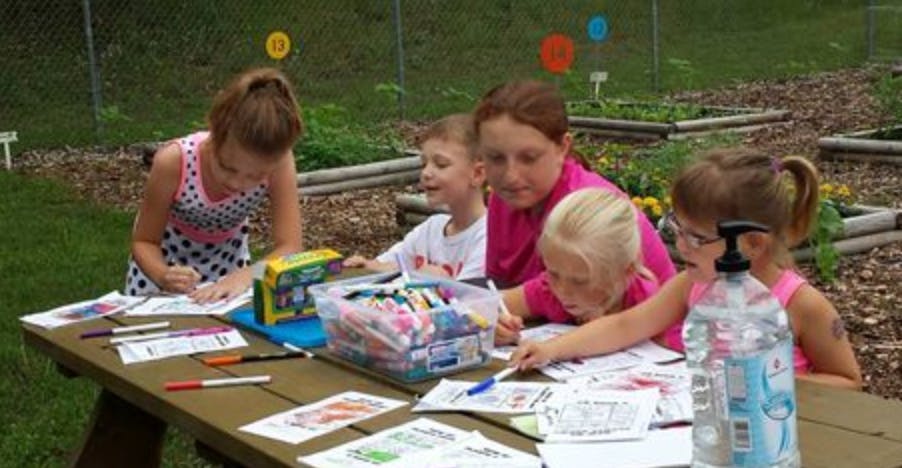 Adult and children drawing and coloring at a table outdoors