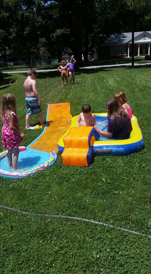 Children playing with an inflatable water slide and pool in a grassy yard