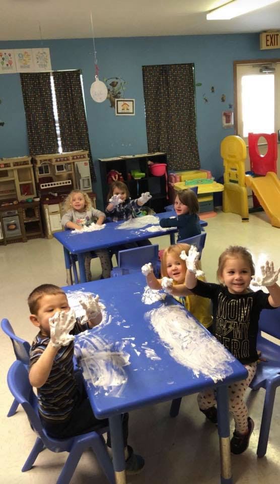 Children playing with white foam at blue tables in a classroom