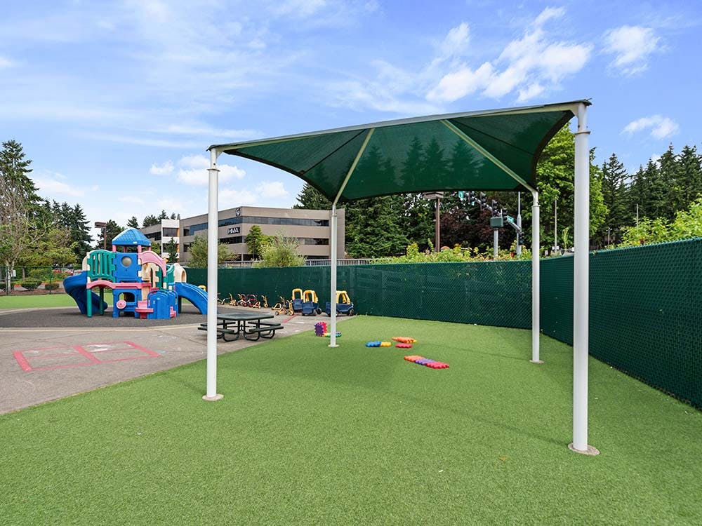 Playground with swings, slides, a green shade cover, and artificial turf