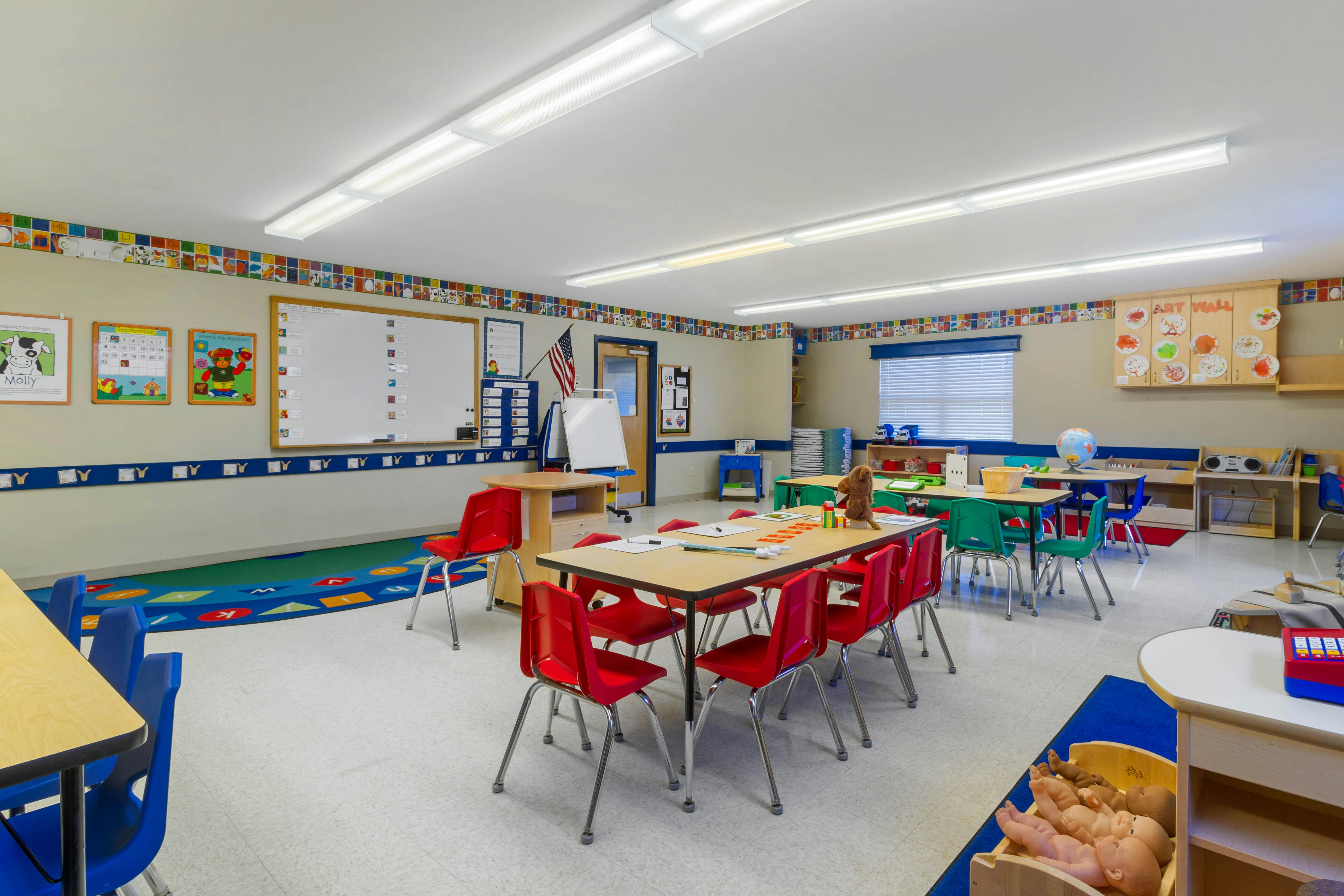 An empty early childhood classroom with multiple tables and chairs