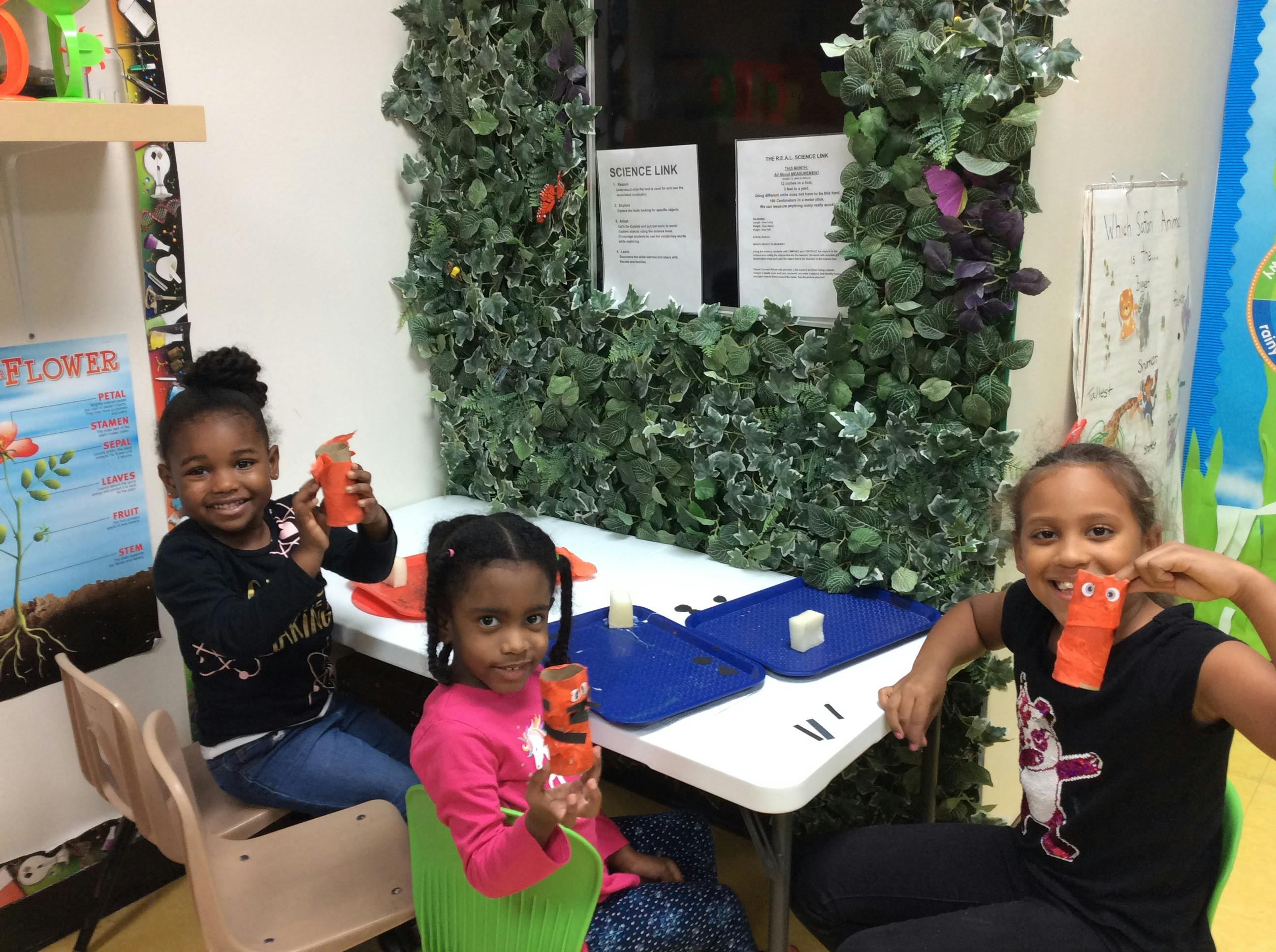 Three children holding orange crafts in a classroom