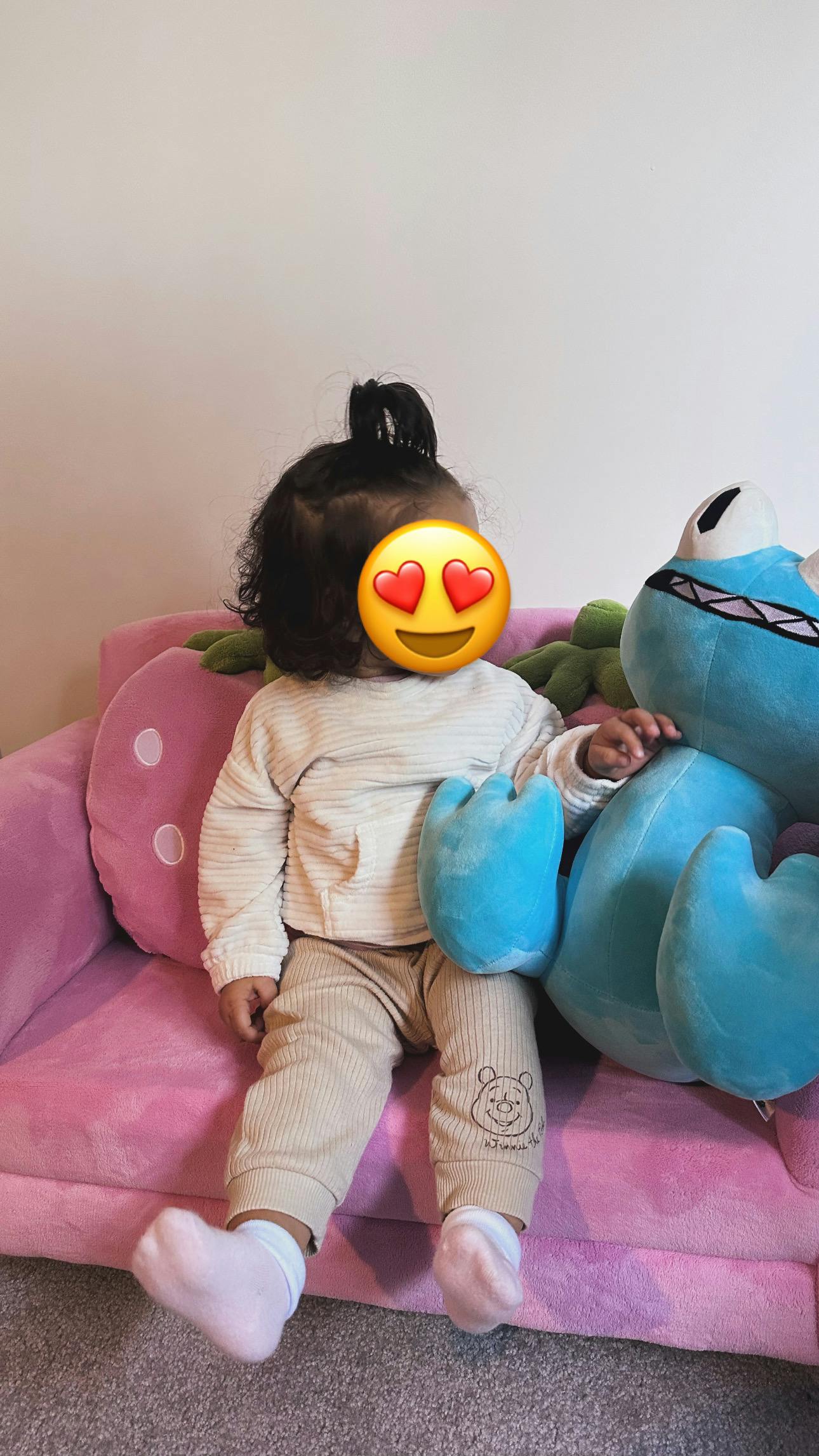 Child sitting on a pink couch next to a large blue stuffed toy