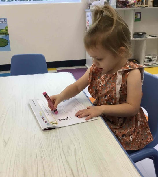 Child sitting at a table writing in a book with a crayon