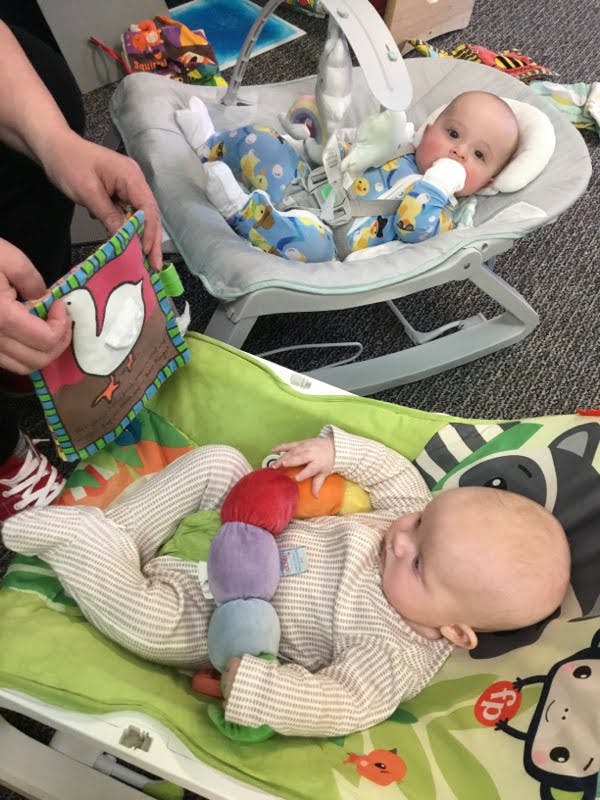 Two infants in baby bouncers, one holding a stuffed caterpillar
