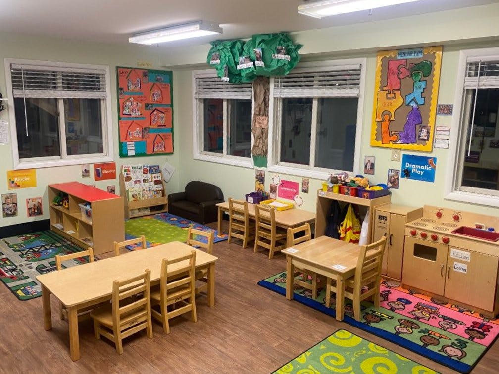 Classroom with child-sized tables, chairs, play kitchen, and rugs