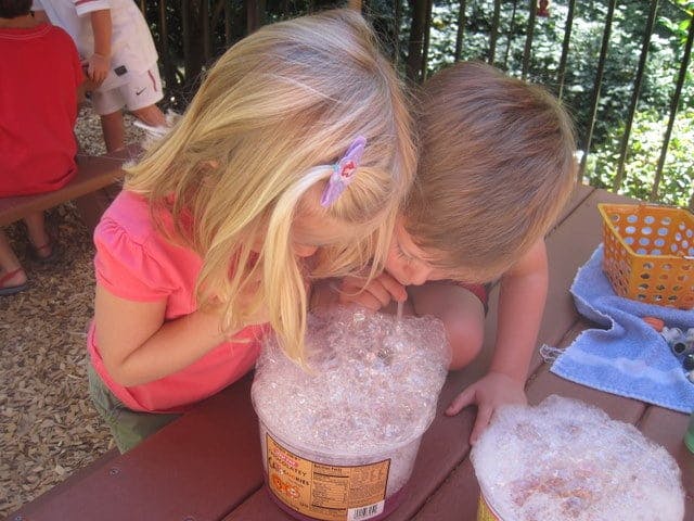 Two children blowing bubbles into containers