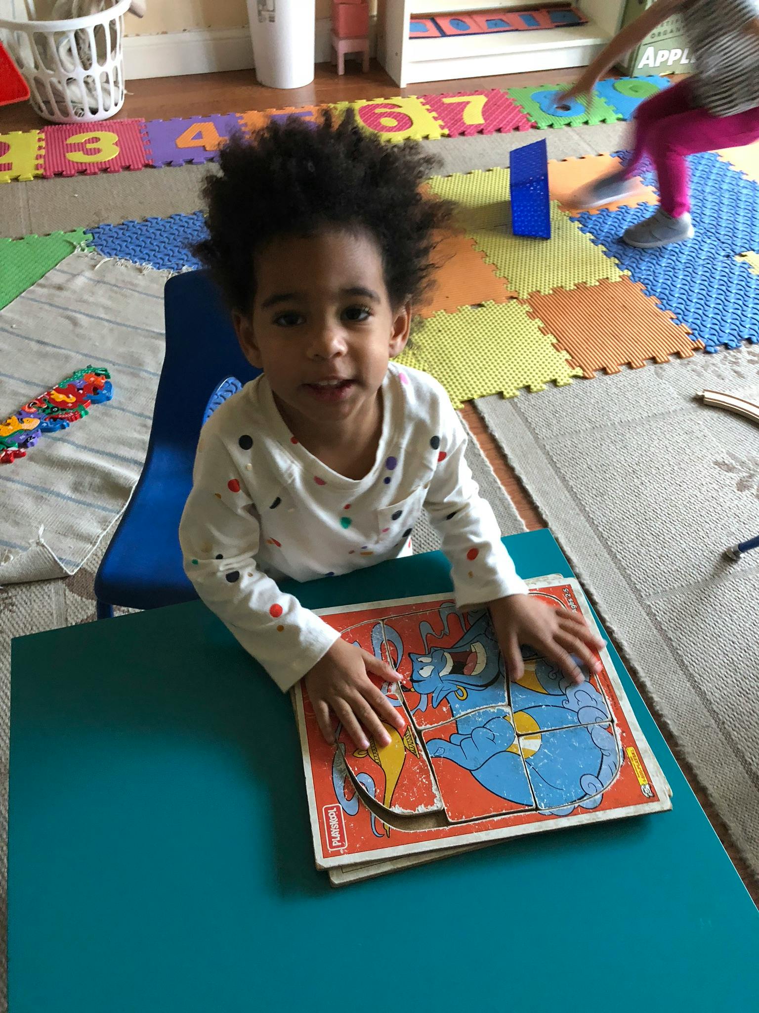 Child sitting at a table with hands on a puzzle