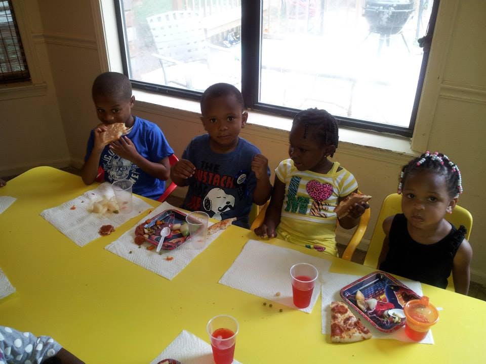 Four children sitting at a yellow table with food and drinks
