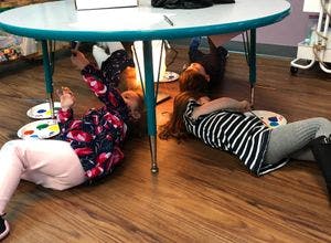 Two children lying on the floor under a table