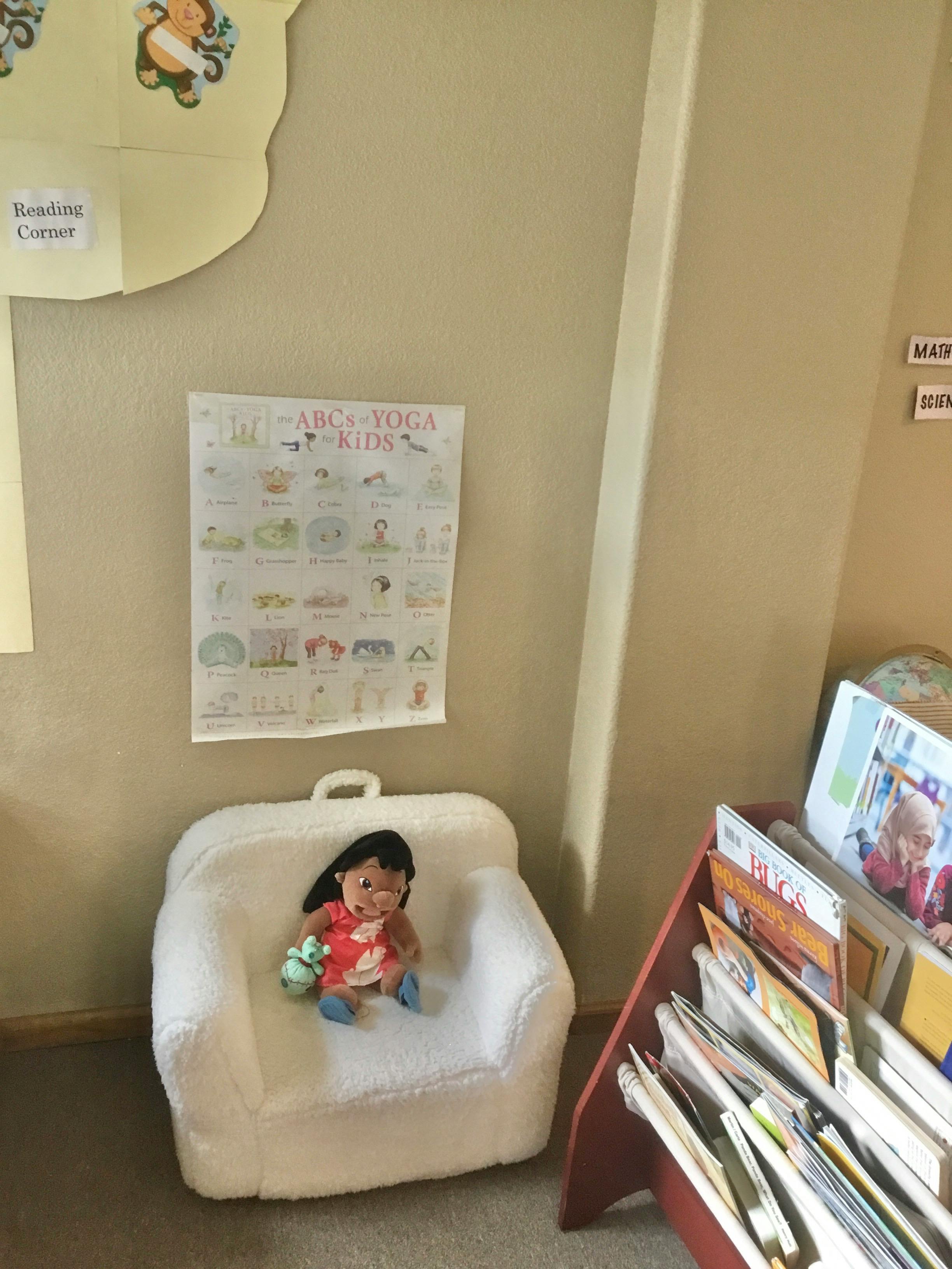 Doll sitting on a white child-sized chair with a yoga poster on the wall