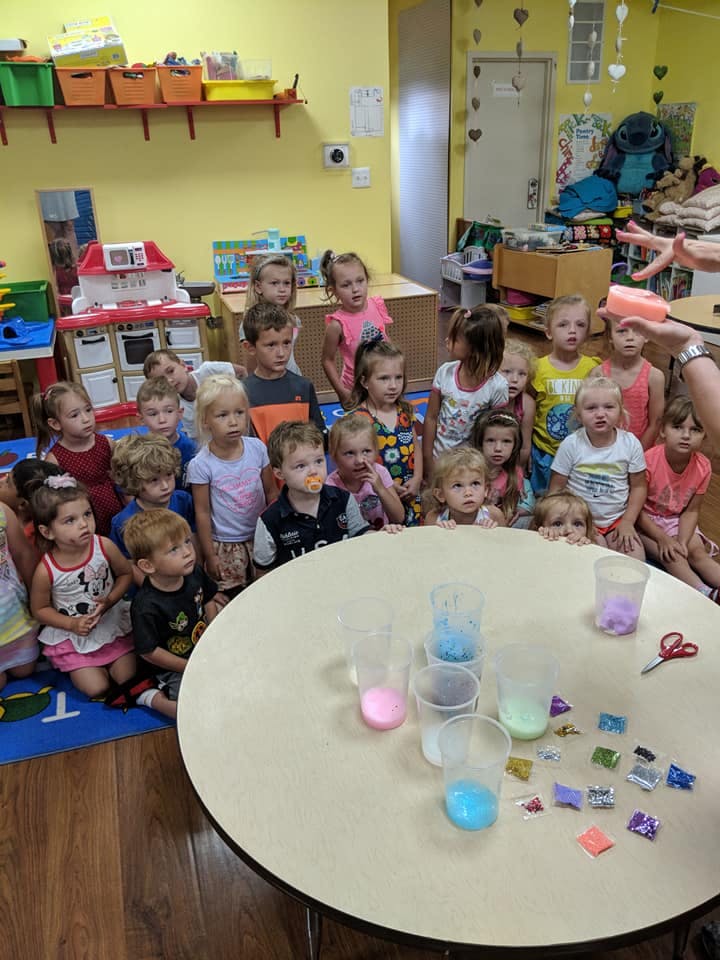 Group of children watching an activity at a table with colorful liquids