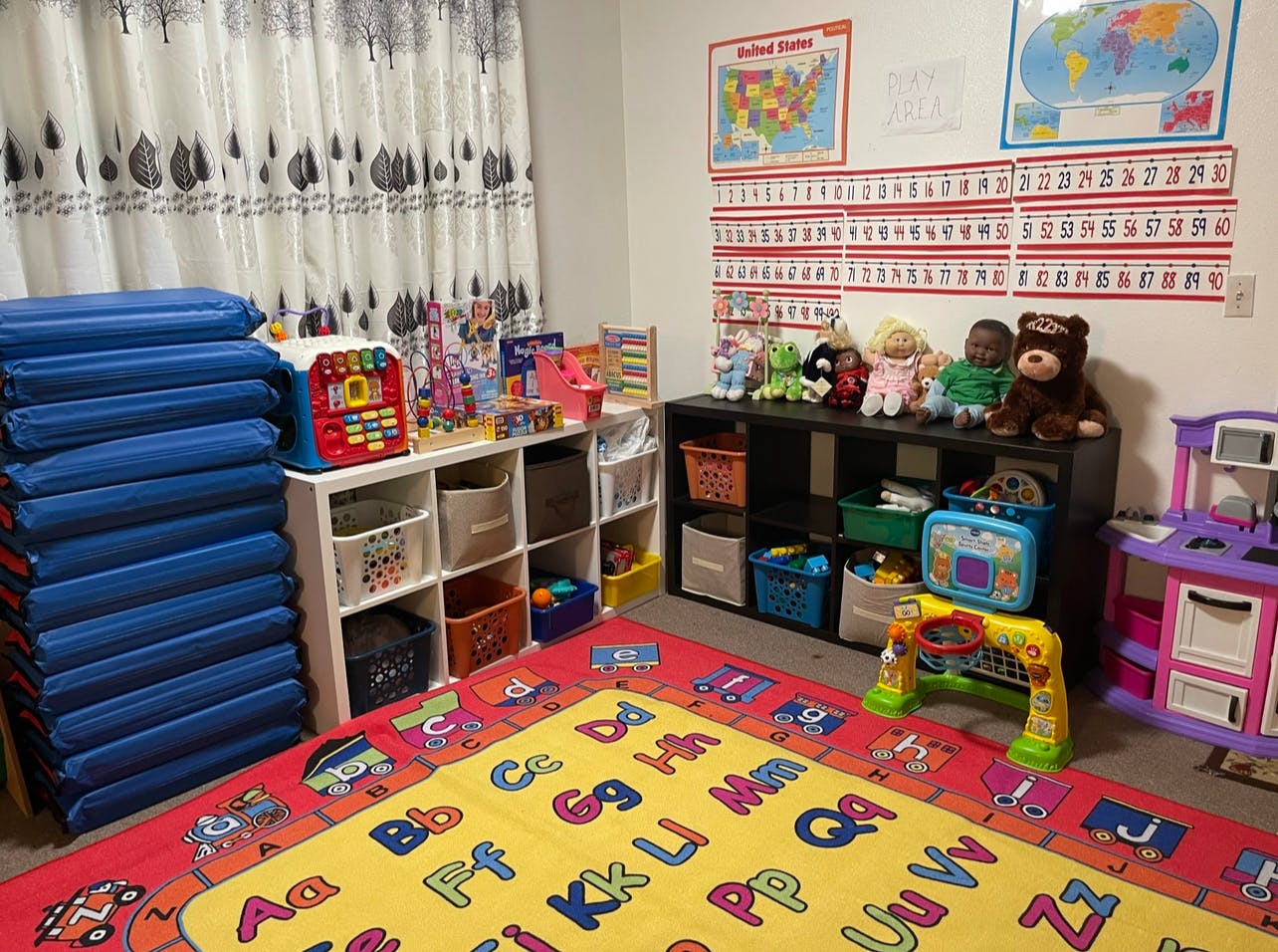 Playroom with alphabet rug, shelves of toys, and blue mats