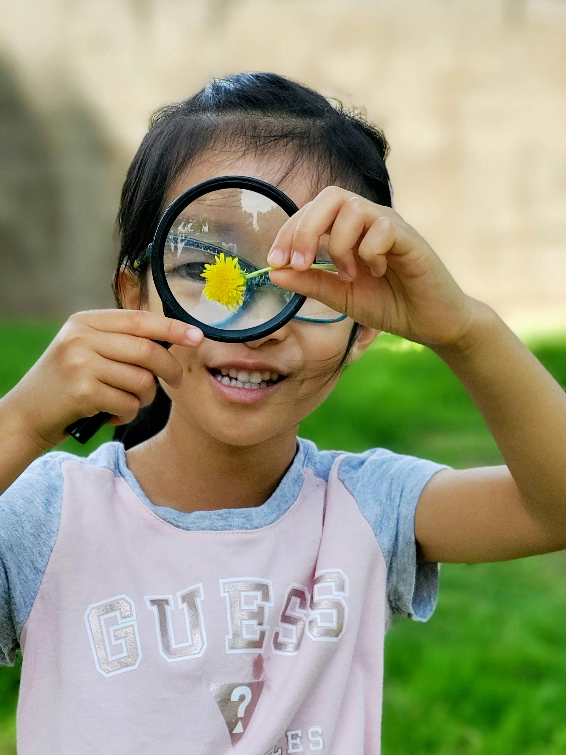 Child holding a magnifying glass with a yellow flower in front of it