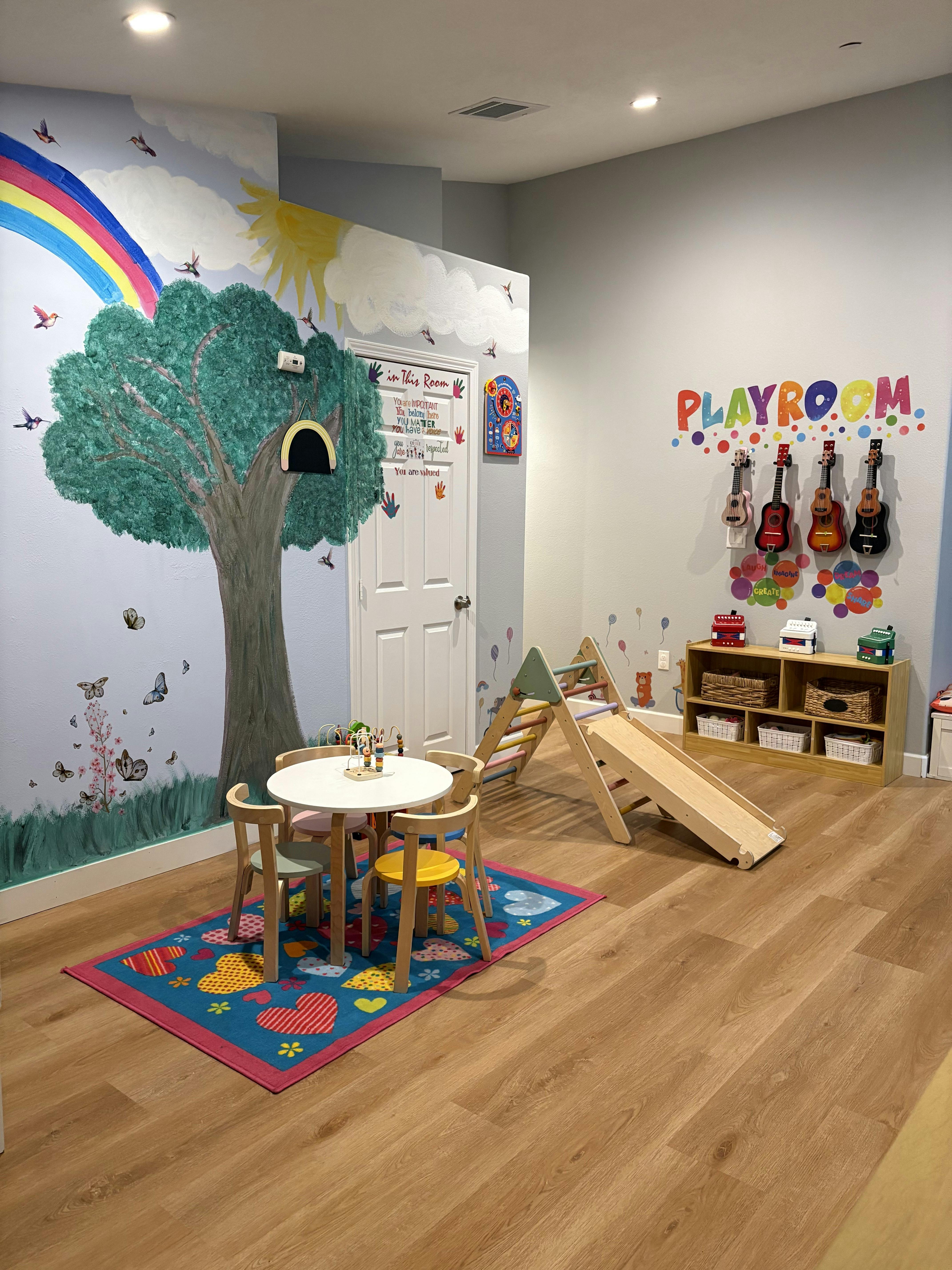 Colorful playroom with mural of rainbow and tree, small table, play slide
