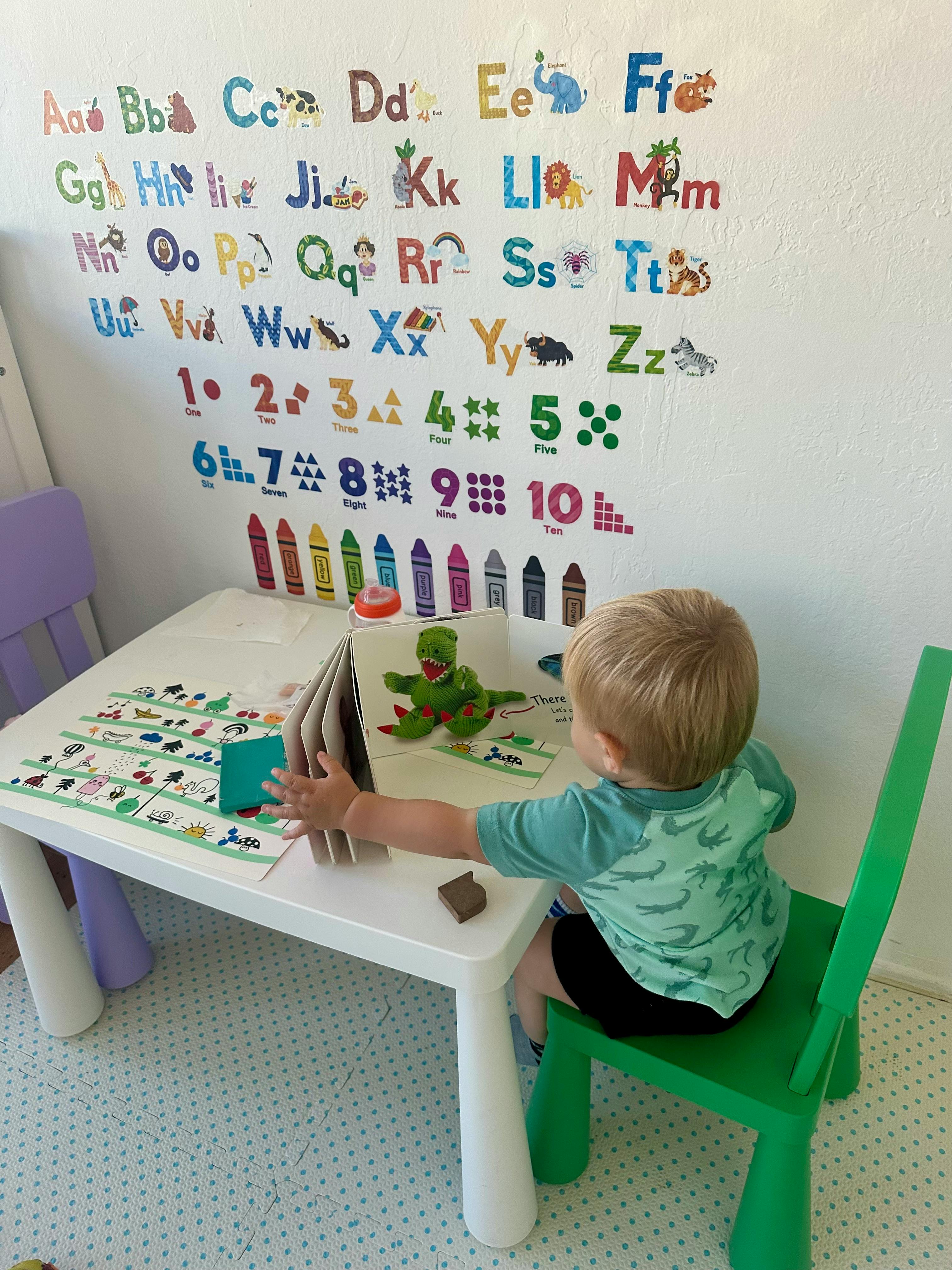 Child sitting at a small table reading a book with a knitted toy