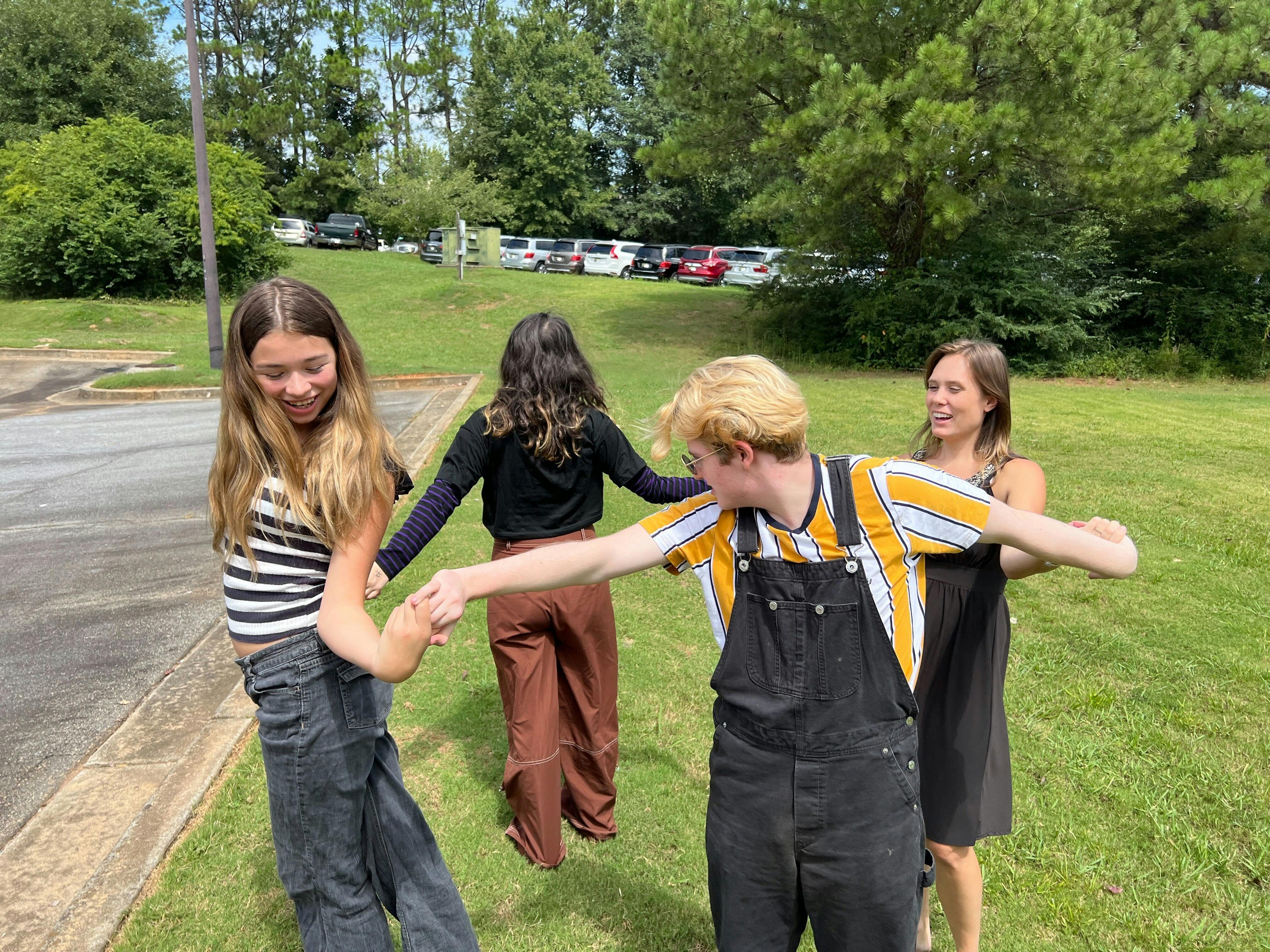 Four people holding hands in a circle on a grassy area