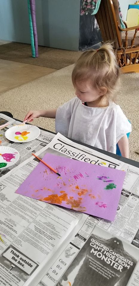 Child painting on purple paper with a paintbrush